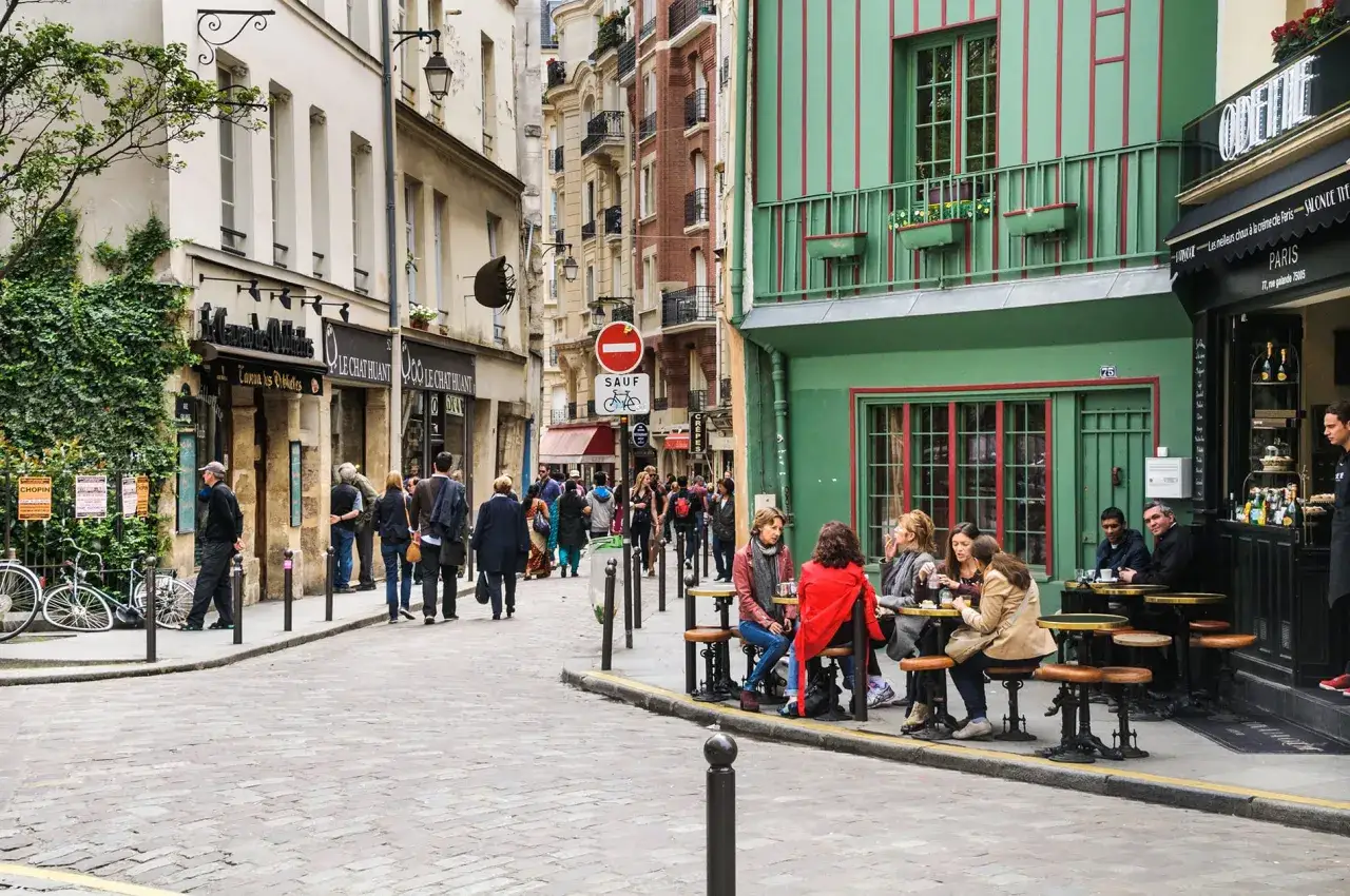 Rue pavée à Paris, des étudiants profitent d'un café en terrasse. Ambiance typique de quartier.