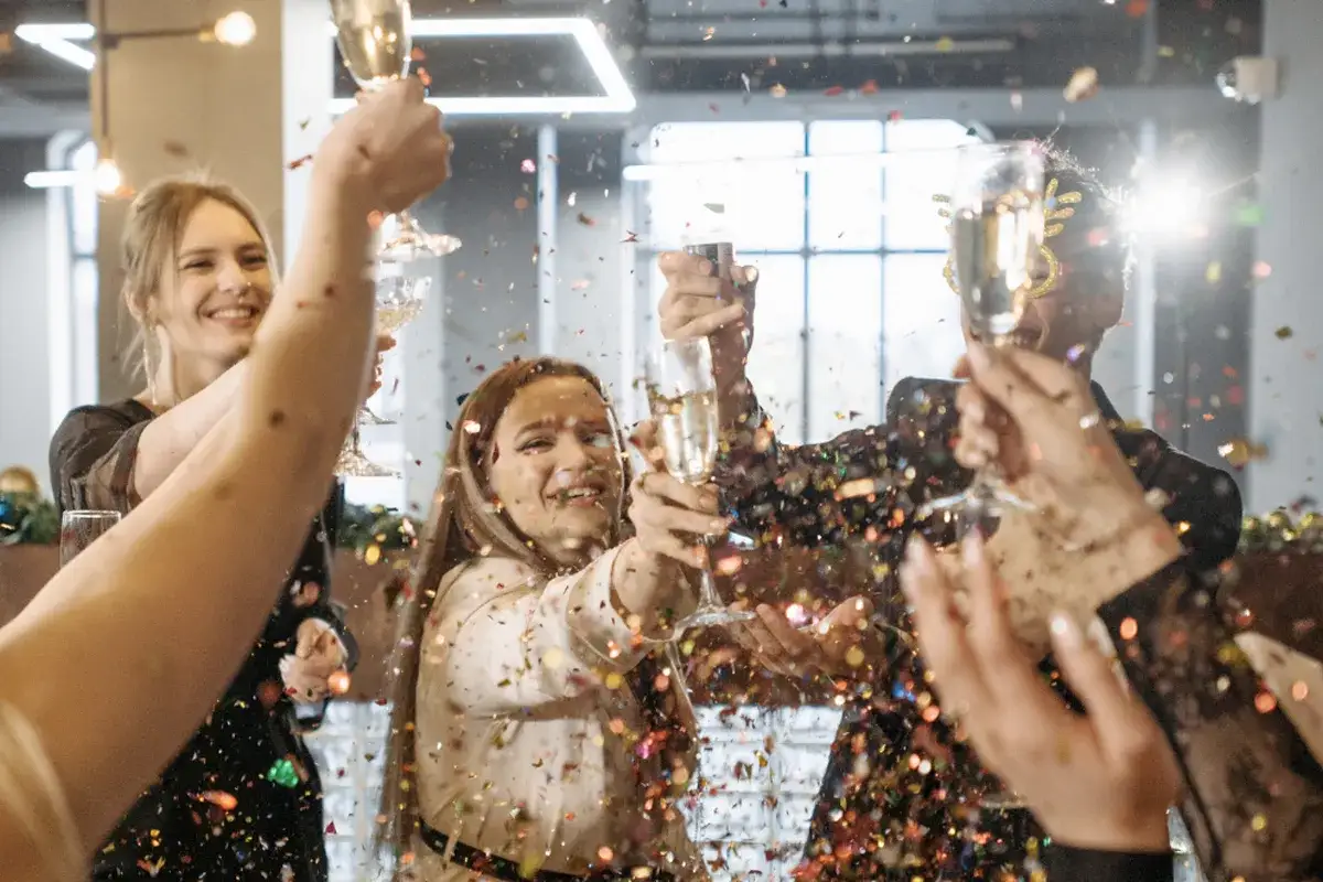 Gente celebrando un aniversario de empresas con confeti y copas de champ&aacute;n.
