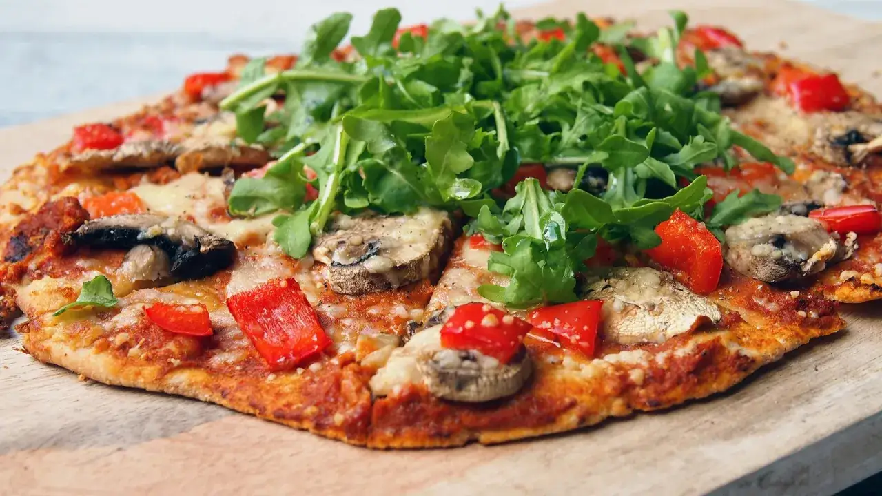 En nyttig pizza med champinjoner, paprika och ruccola p&aring; en tr&auml;sk&auml;rbr&auml;da.