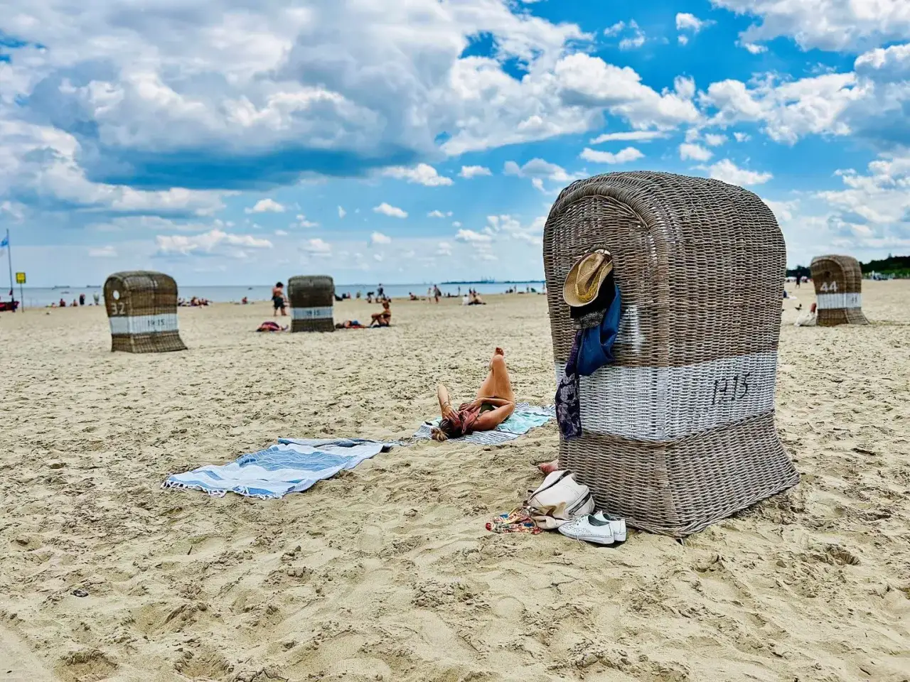 Sopot atrakcje dla dorosłych: plaża z koszami plażowymi, leżakująca kobieta i chmury na niebie.