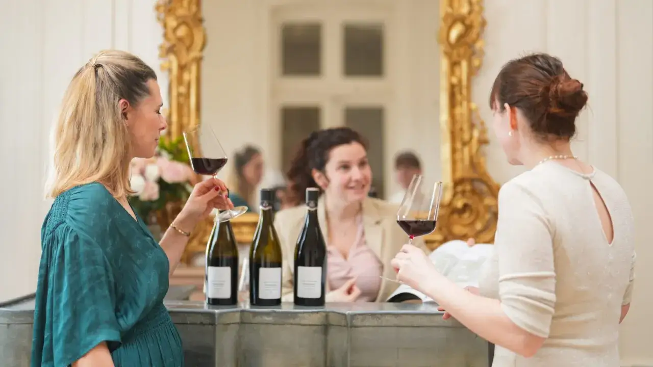 Trois femmes profitent d'une dégustation de vin au Château de Pommard, verres à la main, devant des bouteilles.