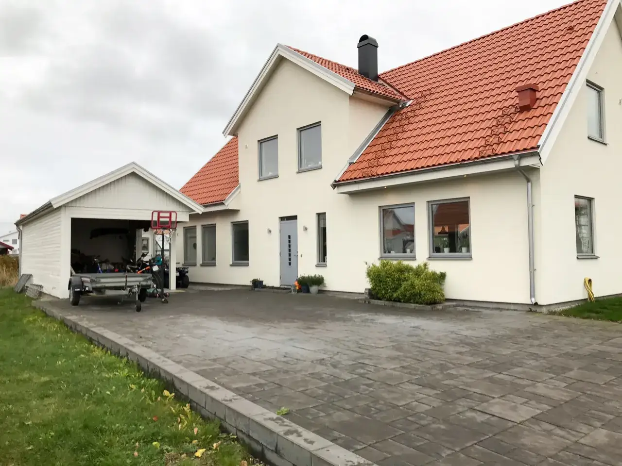 Vitt hus med orange tak och garage. En kamera &ouml;vervakar egen tomt med gr&auml;smatta och uppfart.
