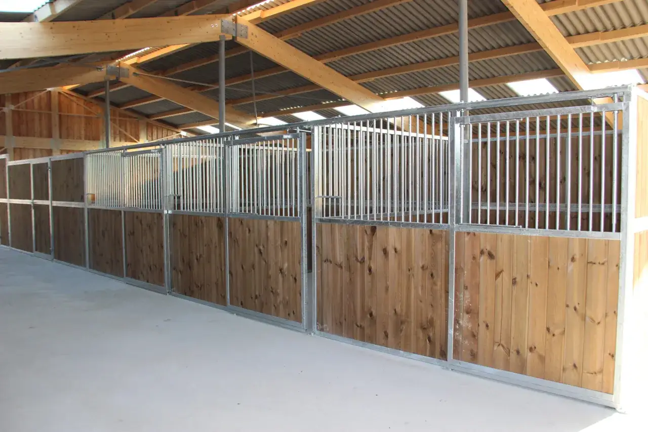 Plan d'un box cheval avec cloisons en bois et barreaux métalliques, sous une charpente en bois.
