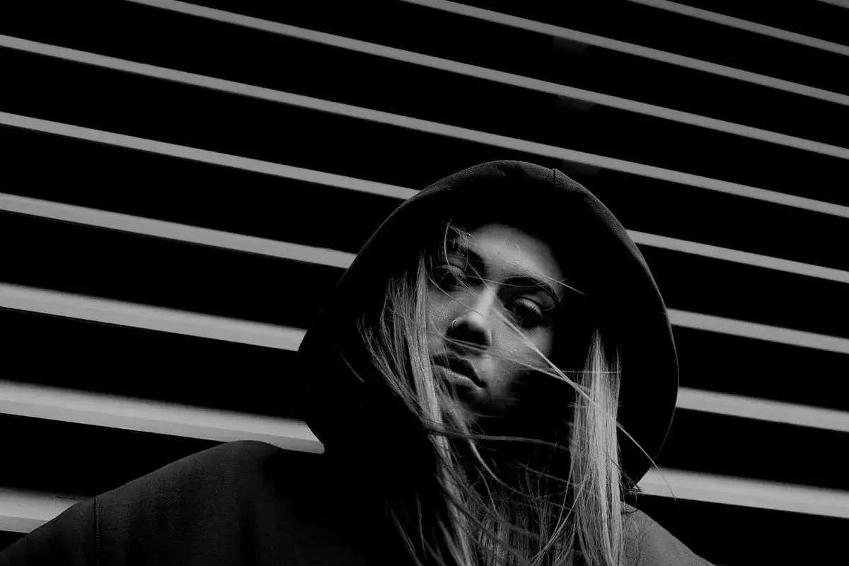Mroczna, czarno-biała fotografia młodej kobiety w kapturze, z rozwianymi włosami. Idealny przykład, jak zrobić czarno białe zdjęcie, by uzyskać taki efekt.