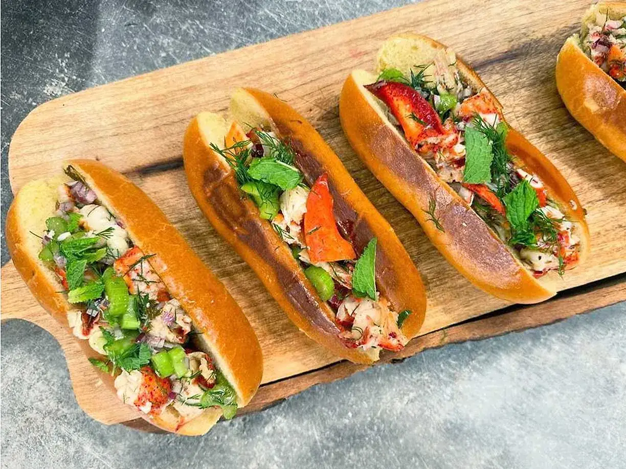 Tre läckra lobster rolls fyllda med saftig hummer, krispig selleri och färska örter, serverade på ett träfat.