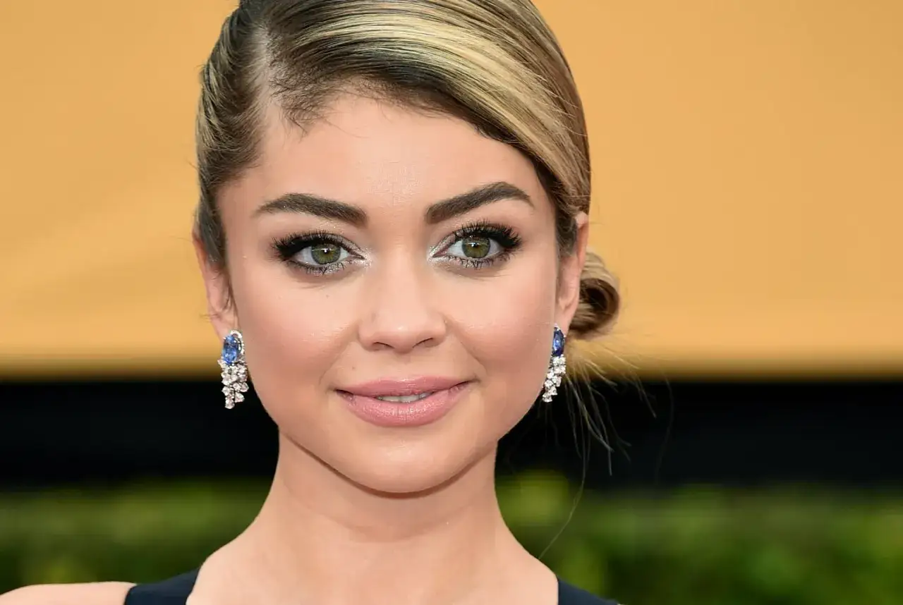 Primo piano di una donna con capelli biondi raccolti e splendidi occhi verde scuro che catturano lo sguardo. Indossa orecchini pendenti con zaffiri e diamanti.