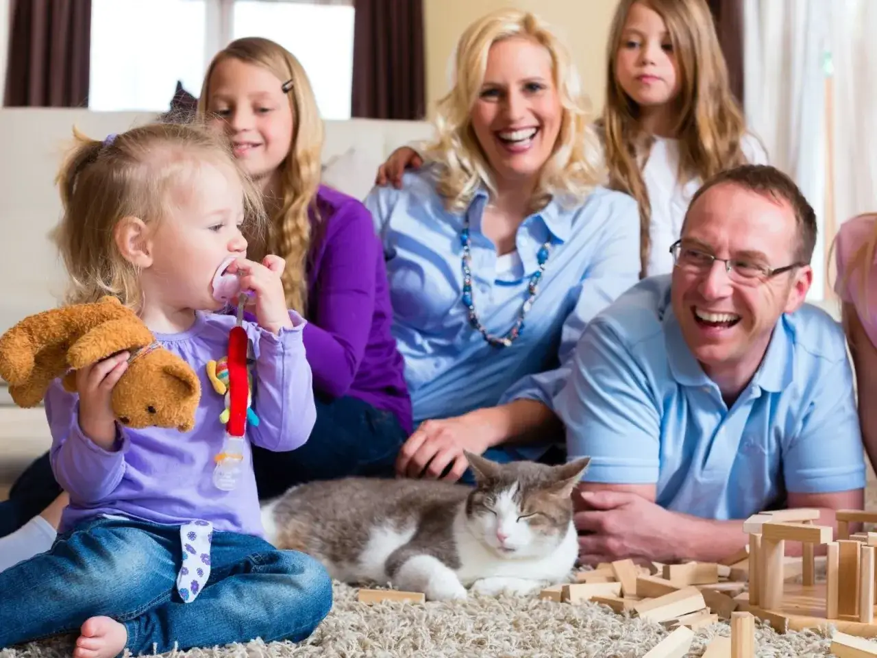 Szczęśliwa mama 4 plus dzieci, tata, kot i klocki na dywanie.
