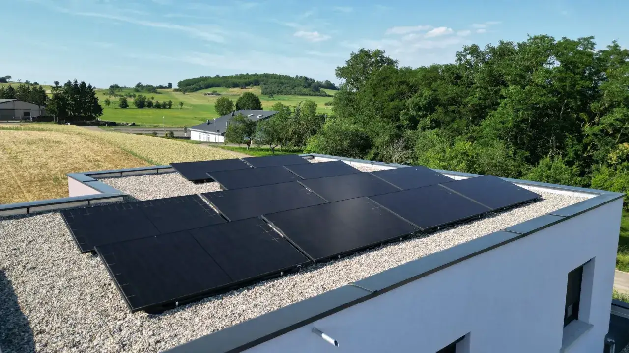 Panneaux solaires noirs sur un toit plat, avec une campagne verdoyante en arri&egrave;re-plan. Une installation qui assure une garantie pour l'avenir.