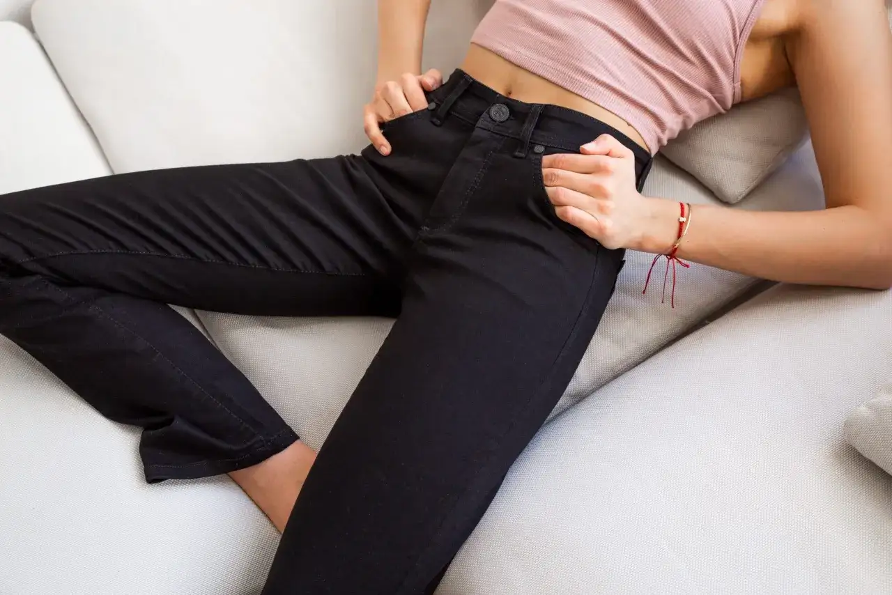 Kobieta w czarnych, dopasowanych spodniach leży na kanapie. Czy jeans się rozciąga? Te spodnie wyglądają na bardzo wygodne i elastyczne.