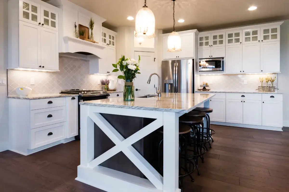 Jasna kuchnia modern farmhouse z wyspą, białymi szafkami i kamiennym blatem.