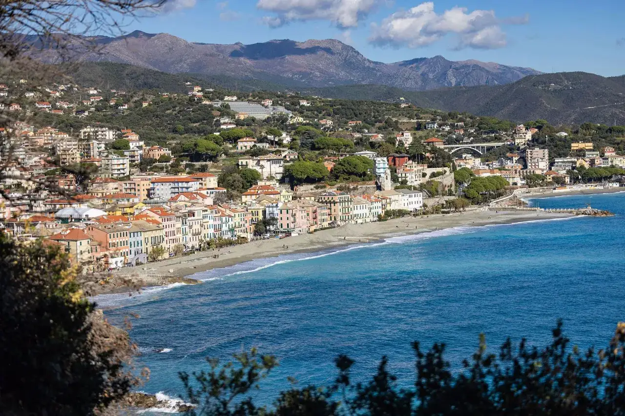 Vue panoramique de Celle Ligure, une ville c&ocirc;ti&egrave;re italienne aux maisons color&eacute;es, bord&eacute;e par une plage de galets et la mer d'un bleu profond.