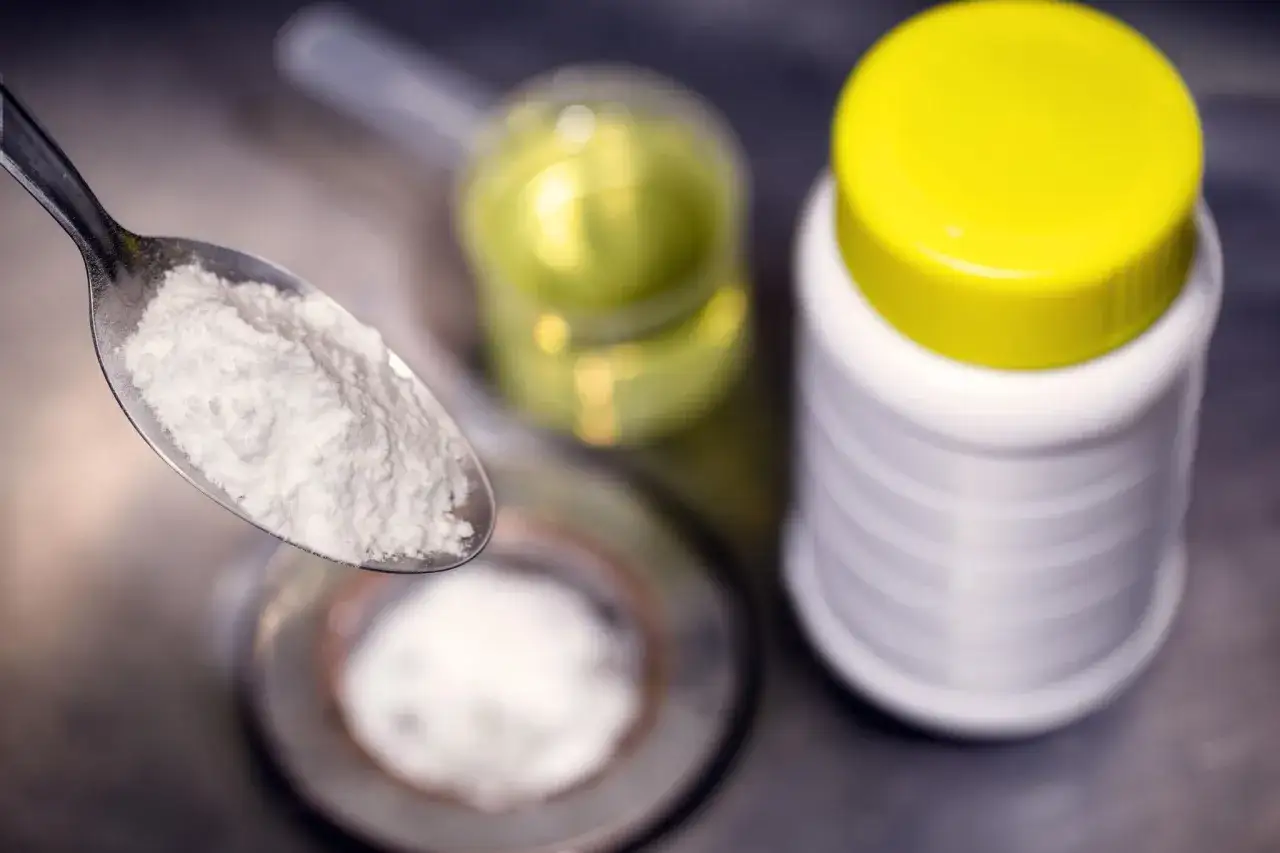 Ein L&ouml;ffel mit wei&szlig;em Pulver, bereit f&uuml;r die Reaktion mit Essig. Daneben ein Beh&auml;lter mit Natron und eine Flasche mit Fl&uuml;ssigkeit.