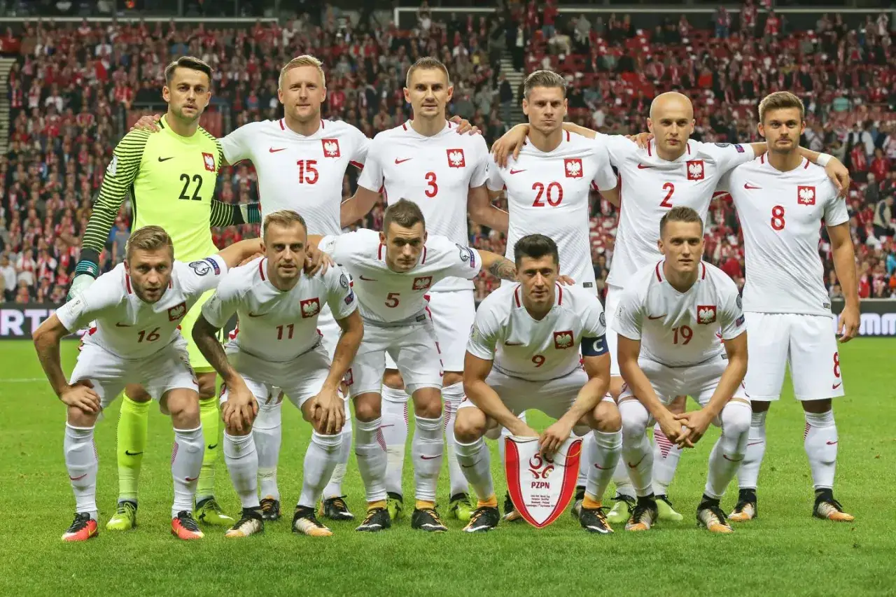 Drużyna piłkarska Polski w białych strojach, gotowa do gry. Wszyscy zawodnicy prezentują dumę z bycia częścią polskiej reprezentacji.