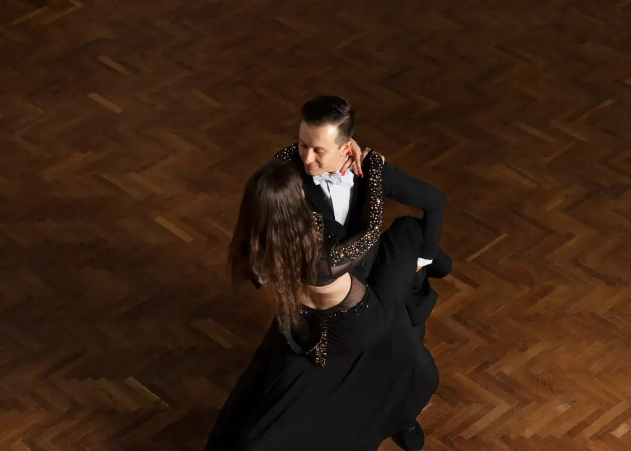 Para tańczy tango argentyńskie, wykonując skomplikowane kroki na drewnianym parkiecie.
