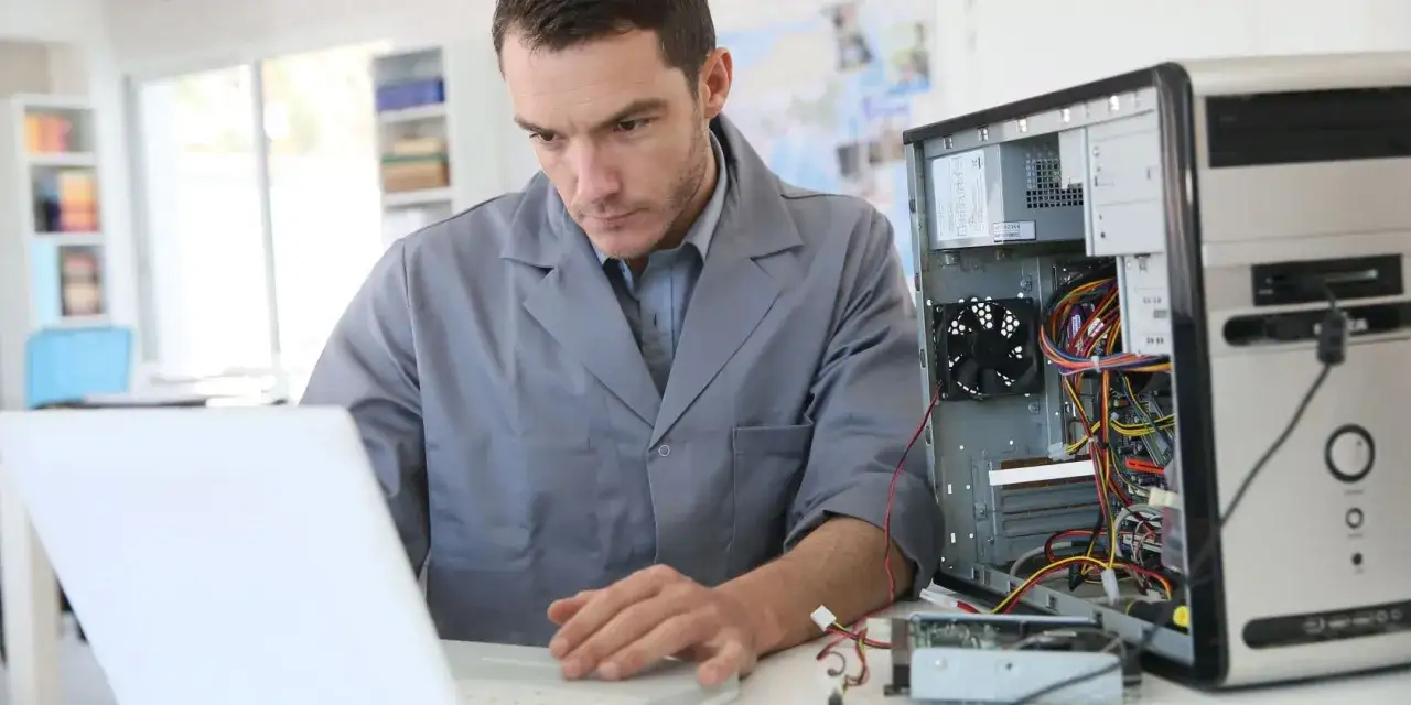 Techniker prüft, warum der PC piept beim Hochfahren. Offener Rechner mit Kabeln und Laptop daneben.