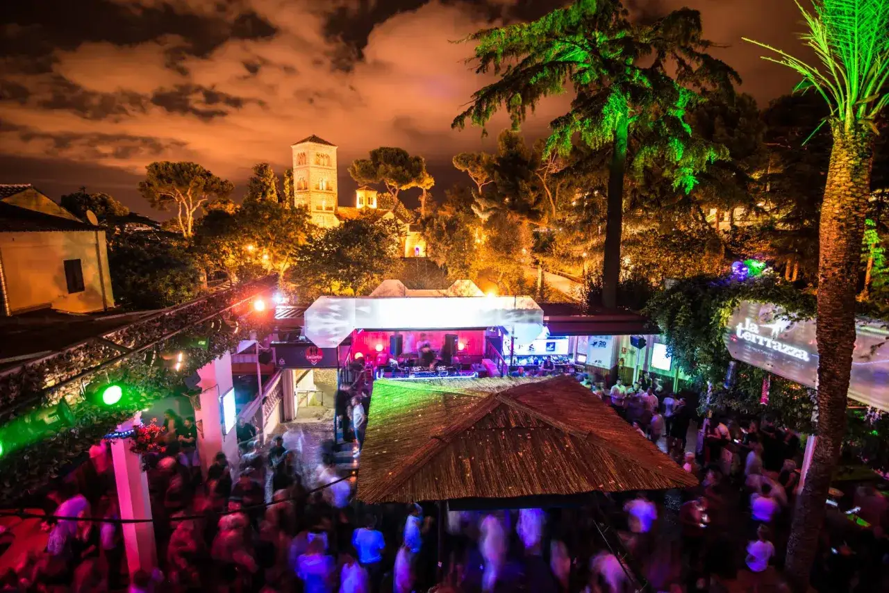 La Terraza Barcelona, una festa notturna con luci verdi e rosa, alberi illuminati e una folla danzante sotto un cielo stellato.