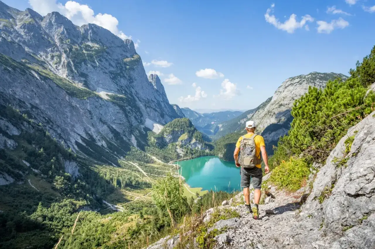 Mężczyzna wyrusza na trekking po Austrii, podziwiając turkusowe jezioro i majestatyczne góry.
