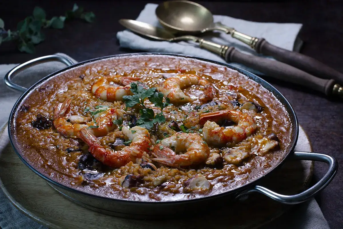 Arroz con pulpo y gambas, un plato de mariscos con arroz cocido en una paellera, adornado con perejil fresco.