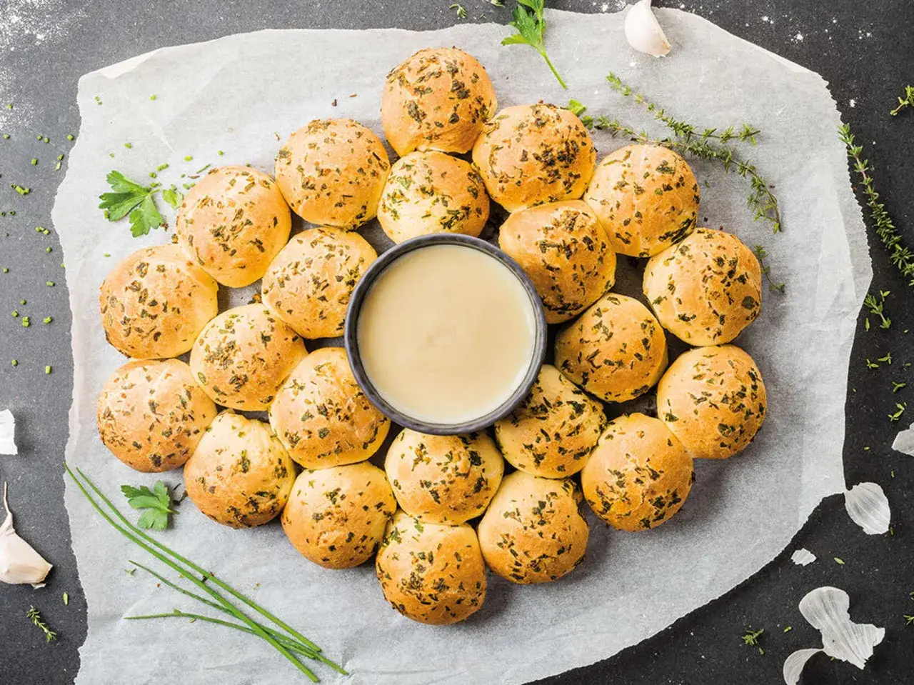 Petits pains dorés aux herbes, disposés en cercle autour d'un bol de sauce crémeuse, évoquant une fondue pyrénéenne.