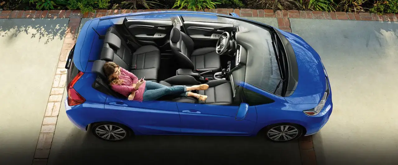 Niebieski Honda Jazz 2 z otwartymi drzwiami, kobieta relaksuje się na tylnym siedzeniu, trzymając telefon.