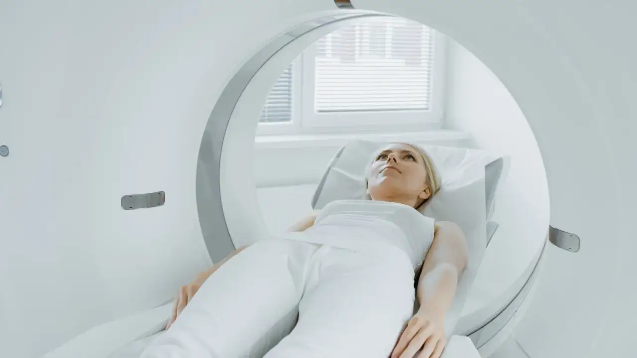 Kobieta leży na ł&oacute;żku w aparacie do rezonansu magnetycznego. Wskaz&oacute;wki, jak przetrwać rezonans magnetyczny, mogą pom&oacute;c w tym badaniu.