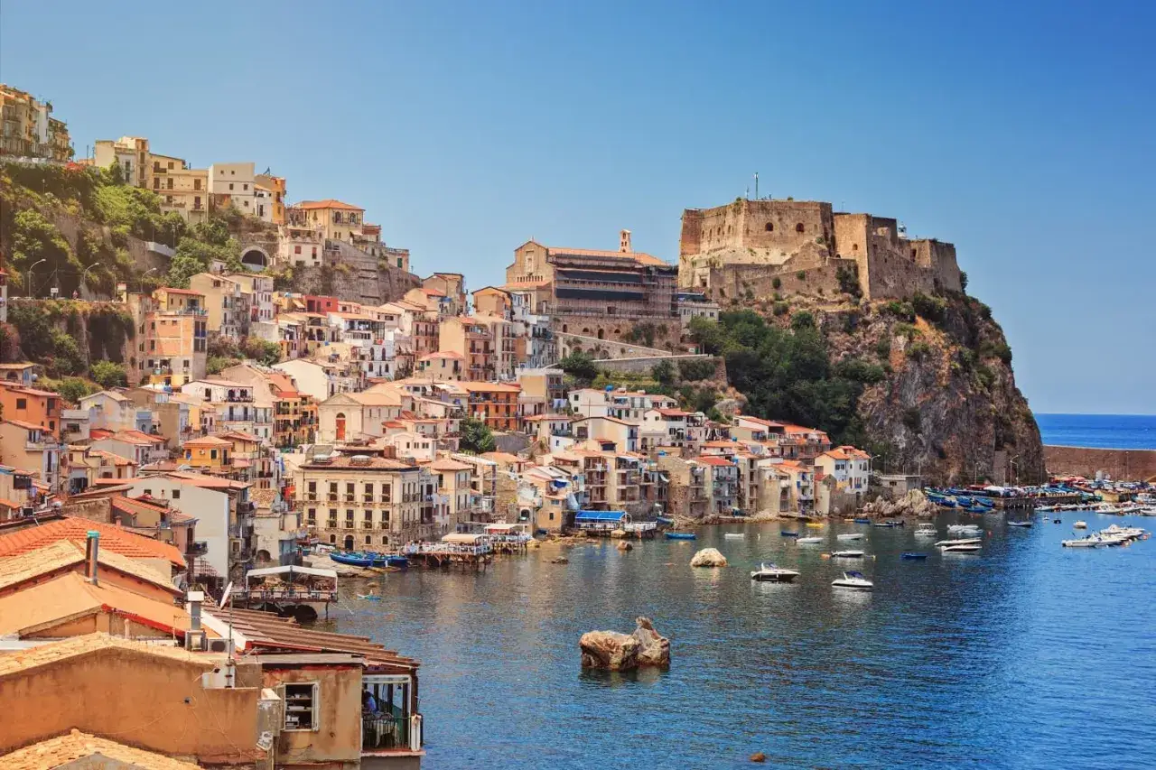 A picturesque view of Scilla, one of the most beautiful Reggio Calabria beaches, with colorful houses cascading down a cliff to a harbor filled with boats.