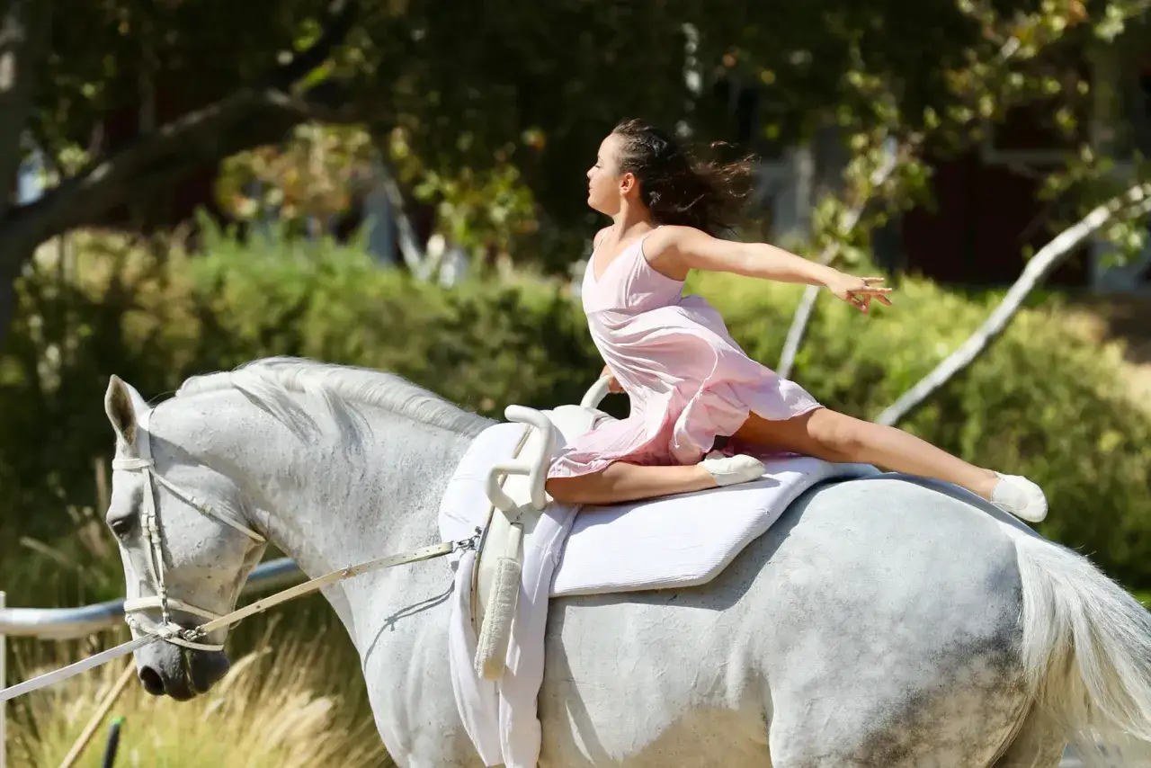 M&auml;dchen in rosa Kleid voltiert auf wei&szlig;em Pferd, zeigt elegante Voltigiere Figuren.