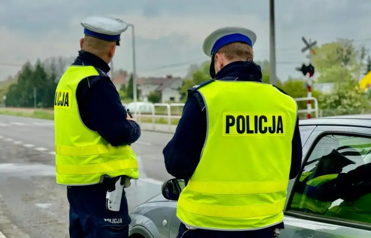 Dwóch policjantów w kamizelkach odblaskowych stoi przy samochodzie. Pilnują porządku i zapobiegają jeździe po alkoholu.