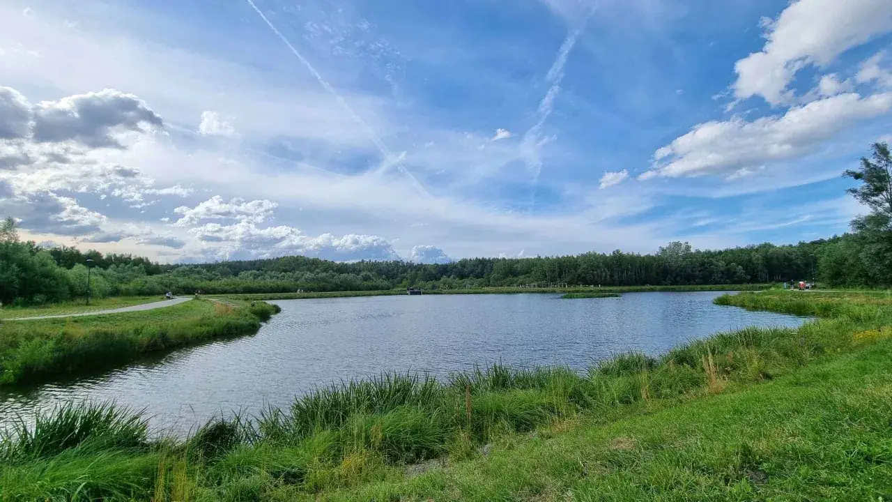 Spokojny akwen w Gdańsku Jasieniu, otoczony zielenią i lasem, pod błękitnym niebem z chmurami.