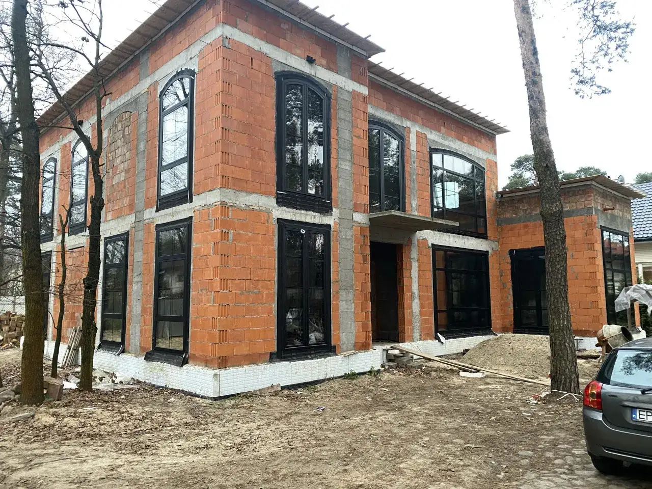 Nowy dom w budowie z czarnymi, nowoczesnymi oknami aluminiowymi. Trwają prace nad montażem stolarki okiennej.
