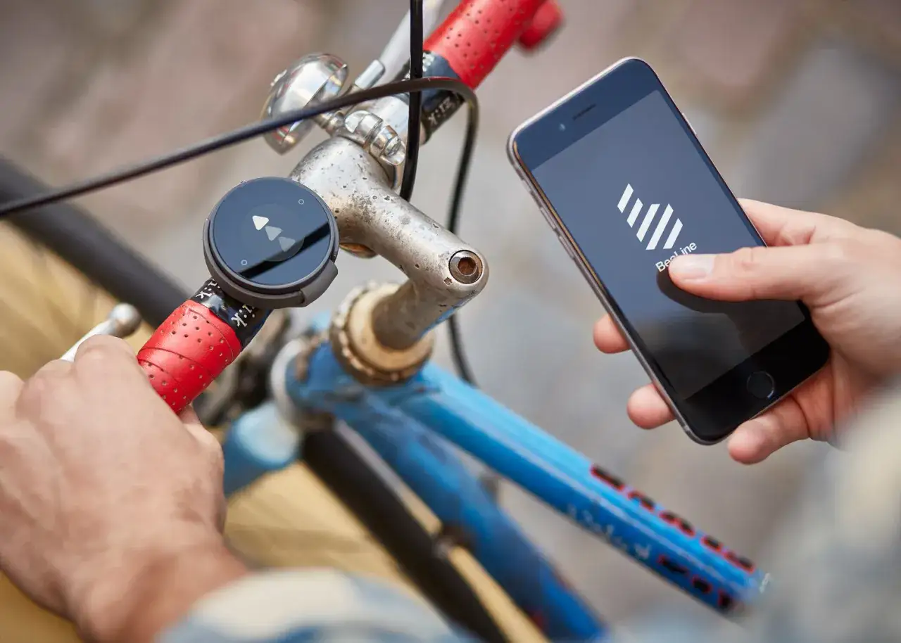 Rowerzysta trzyma iPhone'a z aplikacją na rower, obok zamontowanego na kierownicy urządzenia nawigacyjnego.