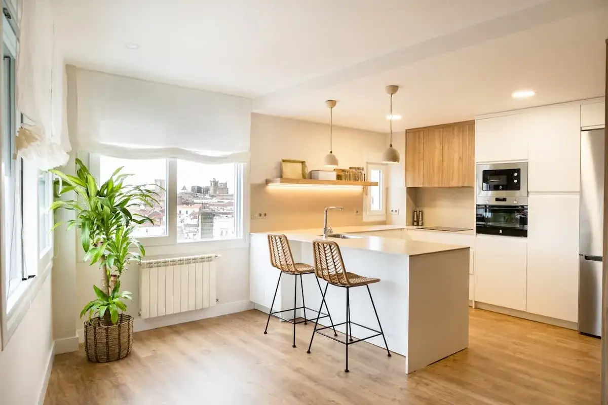 Modernos dise&ntilde;os de cocinas con isla blanca, taburetes de mimbre y vista urbana.