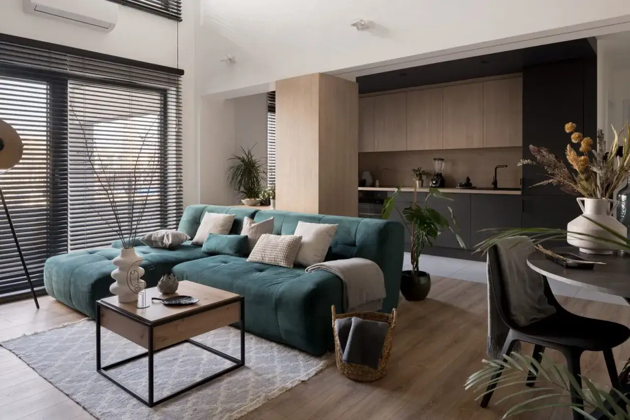 Nowoczesny salon z turkusową kanapą, drewnianym stolikiem i aneksem kuchennym.