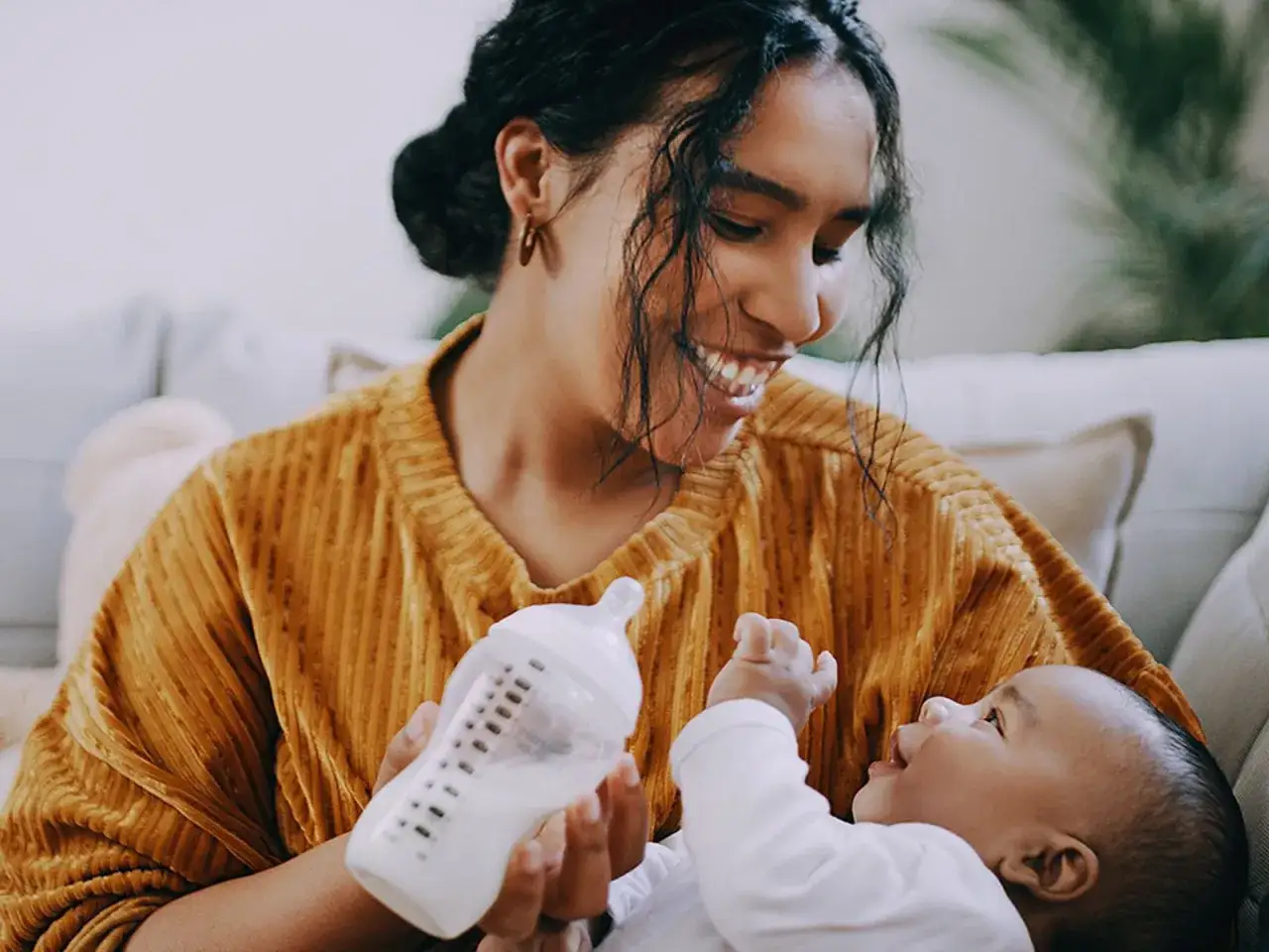 L&auml;chelnde Mutter h&auml;lt eine Flasche f&uuml;r ihr Baby. Sie &uuml;bt paced bottle feeding, um dem Baby zu helfen, die Milch langsamer zu trinken.
