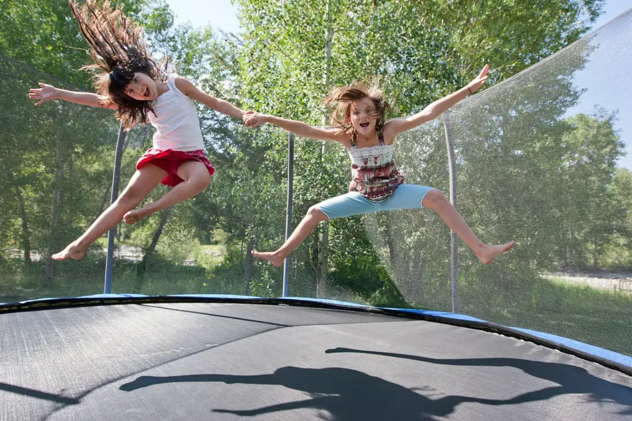 Dwie dziewczynki skaczą na trampolinie, śmiejąc się radośnie. Czy trampolina jest zdrowa dla dzieci? Z pewnością tak, bo to świetna zabawa i ruch!