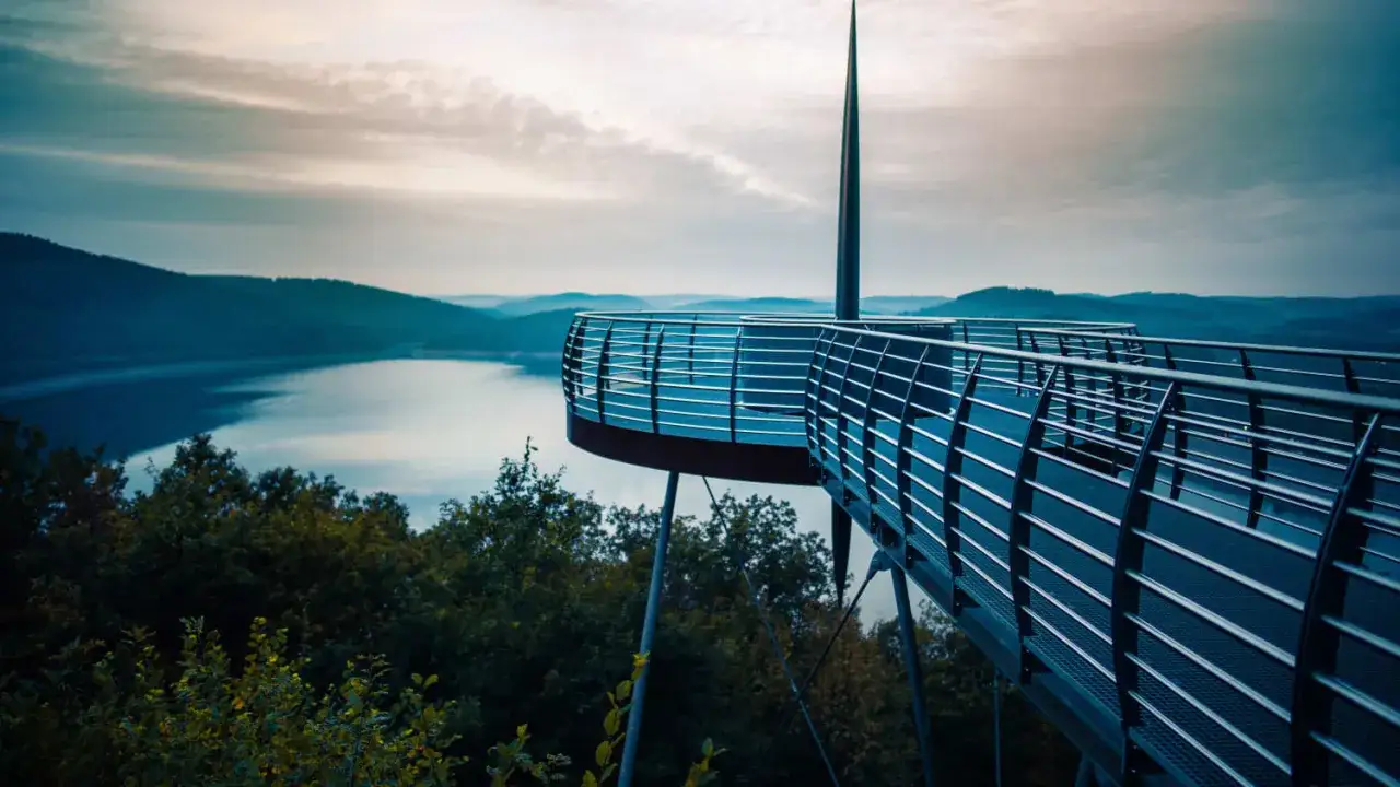 Ein futuristischer Aussichtsturm &uuml;ber einem See in NRW l&auml;dt zum Spazieren gehen ein. Die weite Landschaft mit sanften H&uuml;geln und dem ruhigen Wasser ist atemberaubend.