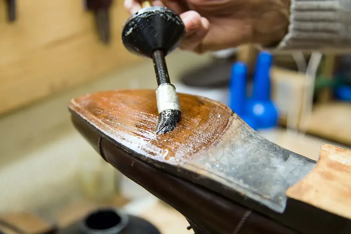 Application de colle sur la semelle d'une chaussure pour sa réparation. Un artisan travaille avec soin.