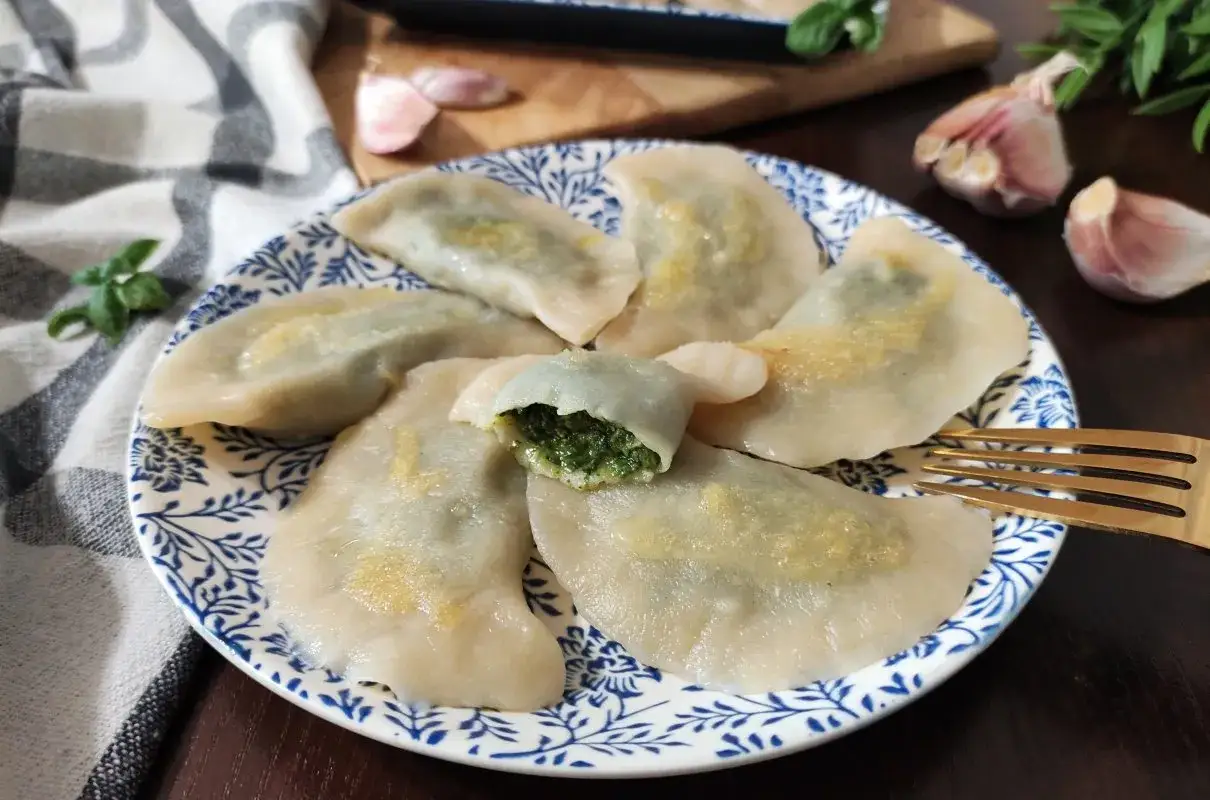 Pyszne pierogi ze szpinakiem i twarogiem, jeden rozkrojony, ukazujący soczyste nadzienie. Obok czosnek i bazylia.