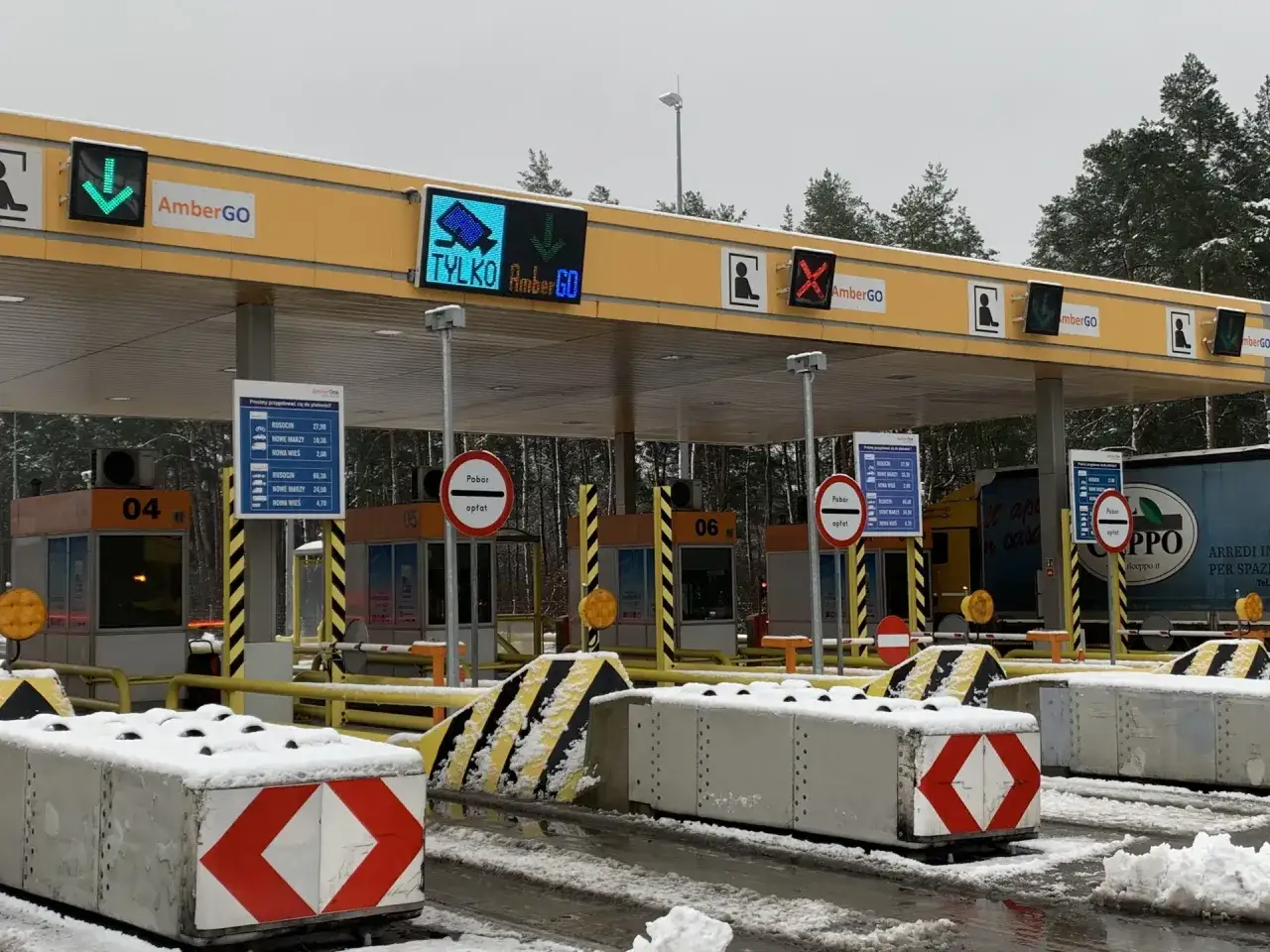 Oznaczenia na bramkach na autostradzie AmberGO: zielona strzałka w dół, czerwony krzyżyk, symbol osoby. Widać tablice z cenami i informacją 