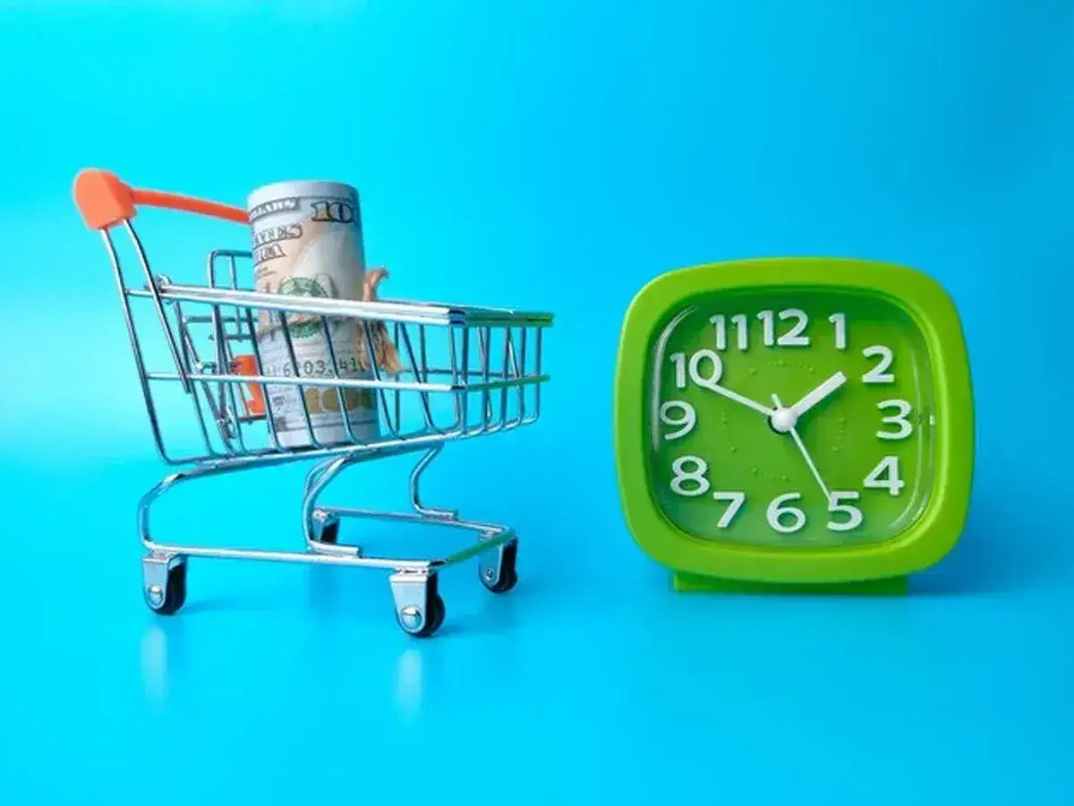 Wózek sklepowy z banknotami i zielony zegar. Hm, ile czasu na zwrot? Czas to pieniądz, a zakupy pochłaniają go szybko.