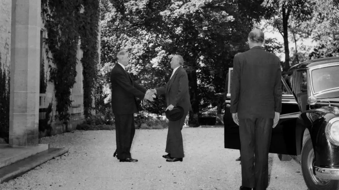 Adenauer und de Gaulle sch&uuml;tteln sich die H&auml;nde. Ein Mann im Anzug steht daneben.