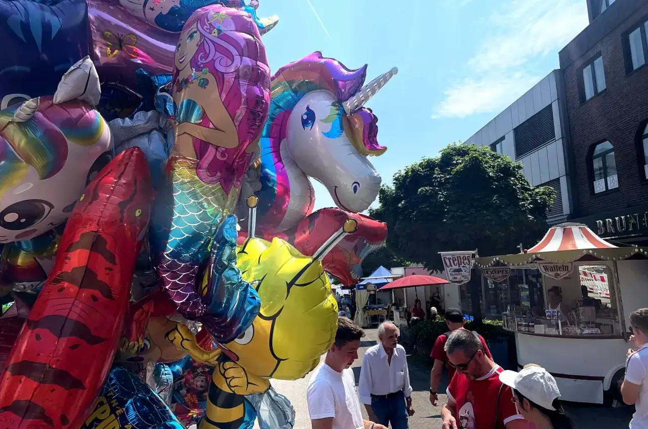 Bunte Ballons mit Einhorn, Meerjungfrau und Biene auf dem Stadtfest Bensberg. Menschen schlendern an St&auml;nden vorbei.