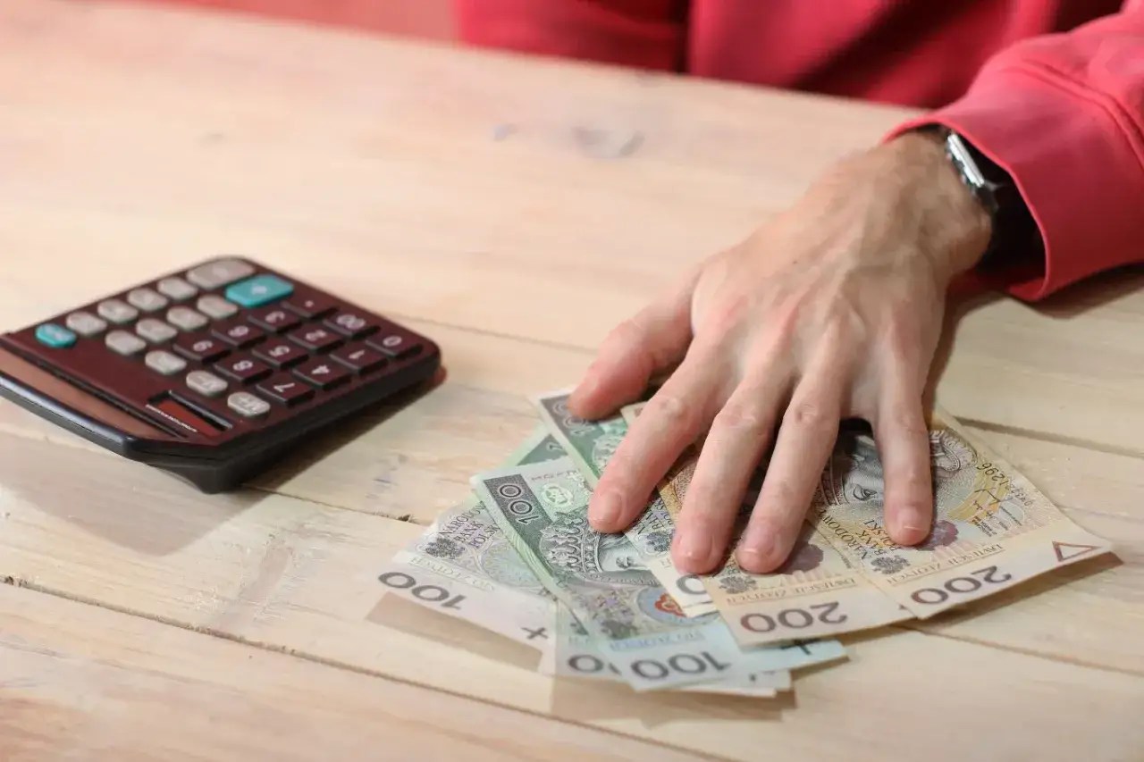 Dłoń nad polskimi banknotami i kalkulatorem. Zastanawiasz się, gdzie zgłosić pracę na czarno?