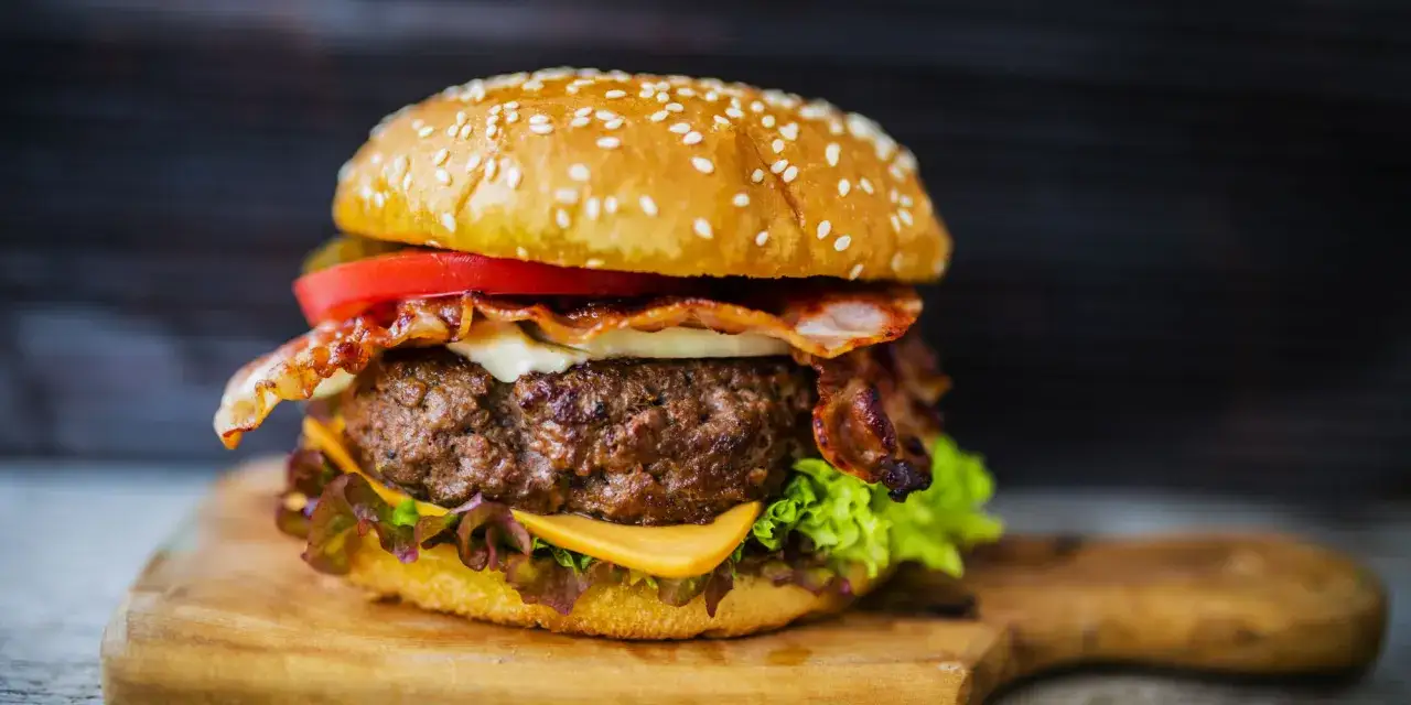 Hamburger di carne succulento con bacon croccante, formaggio fuso, pomodoro e lattuga su un panino ai semi di sesamo.