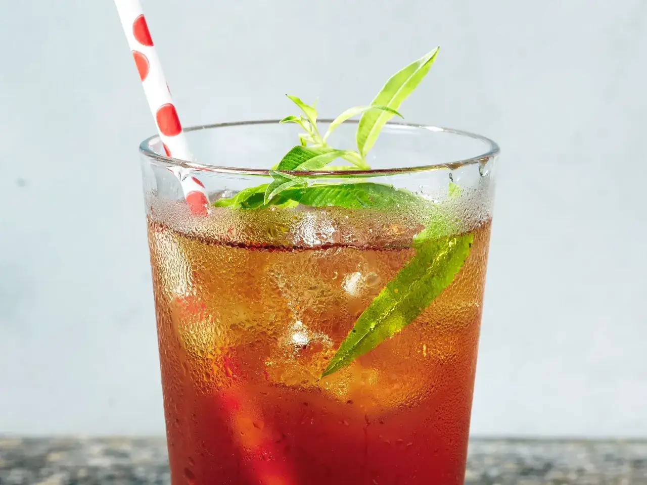 Verre de thé glacé rafraîchissant avec des feuilles vertes et une paille à pois. Découvrez les mugicha bienfaits pour une boisson saine.