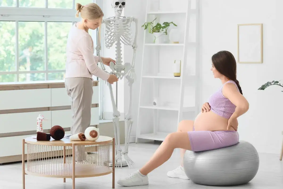 Gravid kvinna med foglossning kan inte gå. Fysioterapeut visar bäckenet på ett skelett.
