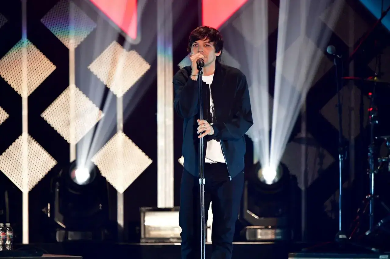 Louis Tomlinson na scenie, śpiewa do mikrofonu. W tle efektowne oświetlenie i dekoracje. Fani czekają na kolejne louis tomlinson nadchodzące wydarzenia.
