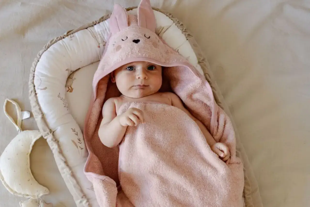 S&ouml;t baby i en rosa badcape med kanin&ouml;ron, mysigt inb&auml;ddad i en babynest.