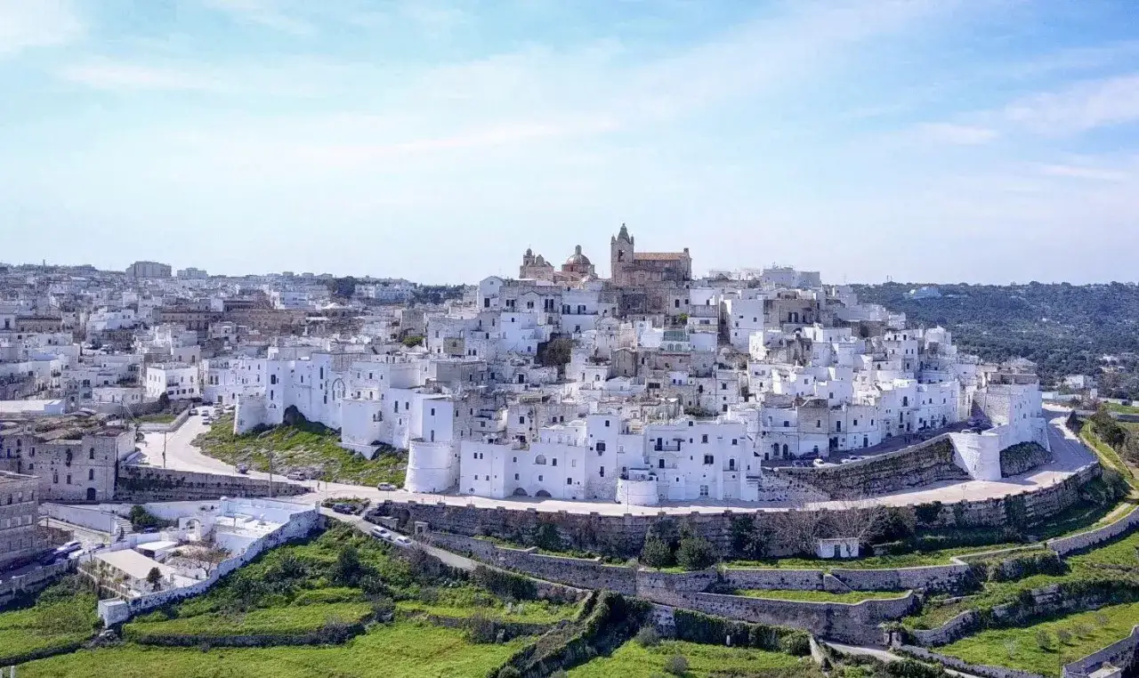 Un borgo bianco arroccato su una collina, con chiese e case che si affacciano su un paesaggio verde. Un'ottima meta per scoprire l'entroterra Salento cosa vedere.