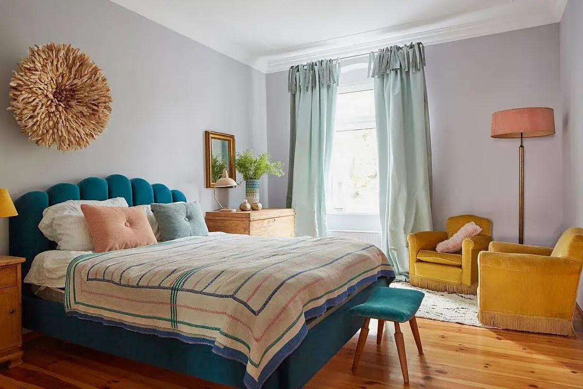 A small maximalist bedroom with a teal bed, patterned throw, and a large feathered wall hanging.